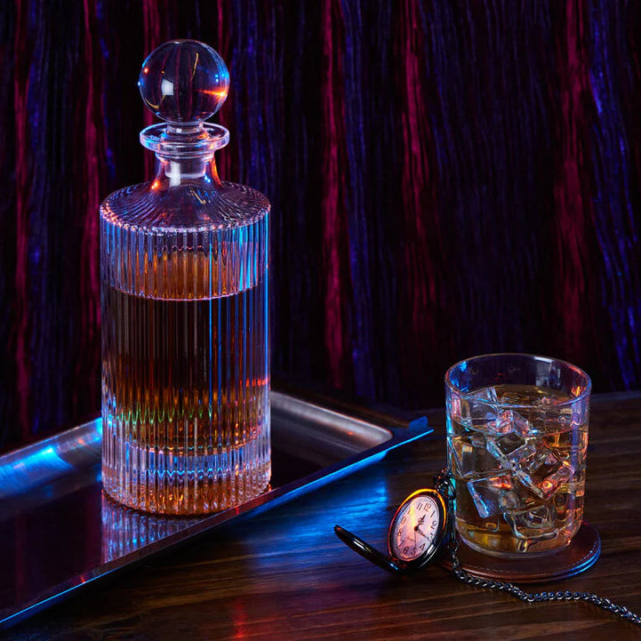 Alcohol decanter and glass with ice on a tray against a dark background
