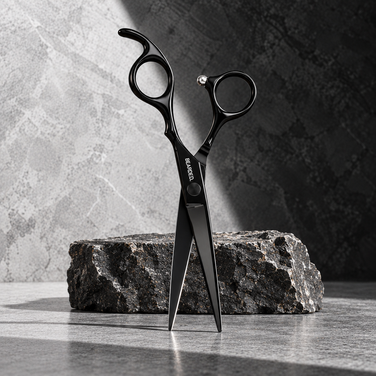 Black professional hair shears standing upright on a dark textured stone block against a gray stone wall background.