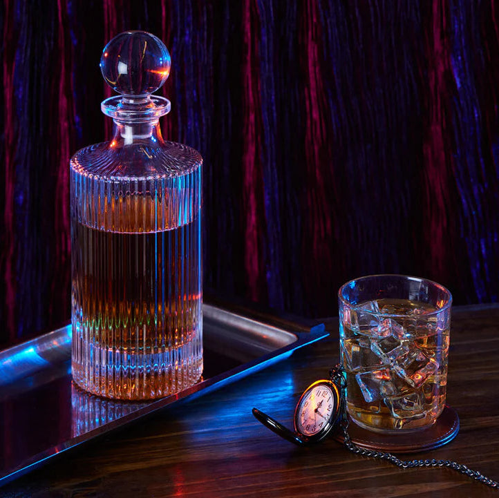 Alcohol decanter and glass with ice on a tray against a dark background